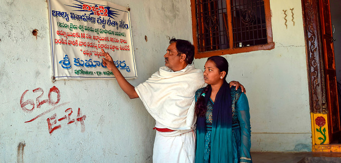 Den hinduiske prästen Shri Kumar Sharma visar tillsammans med sin dotter på den varning mot bortgifte av barn som sitter utanför hans kontor. Foto: Stella Paul/IPS.