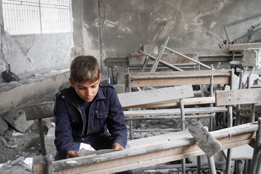 En syrisk pojke läser på ett trasigt papper i sitt gamla förstörda klassrum i Aleppo, november 2012. Foto: AP/TT.